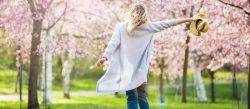 Young woman dancing in park holding hat during spring time.